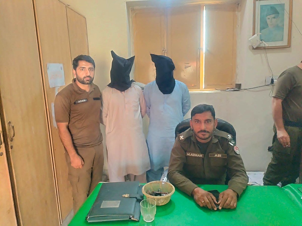 Two arrested suspects with police officials at a Faisalabad police station