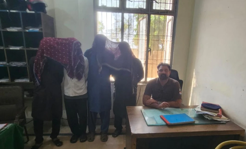 Faisalabad shop theft gang: hooded accused in custody with policeman.