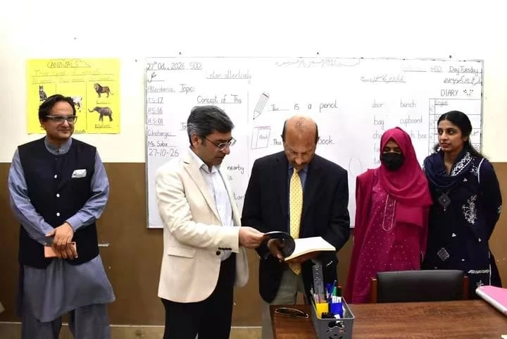 The vice chancellor looks at a book with teachers in a classroom